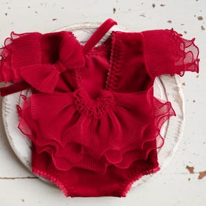 May include: Red ruffled baby outfit with a matching headband. The outfit has a layered ruffle design and a bow on the front.