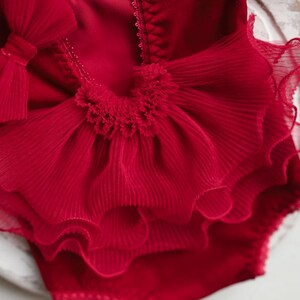 May include: Red ruffled baby bodysuit with a large bow on the front. The bodysuit is made of a soft, delicate fabric and is perfect for a special occasion.