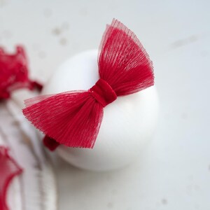 May include: A red tulle bow headband with a velvet center. The headband is on a white surface.