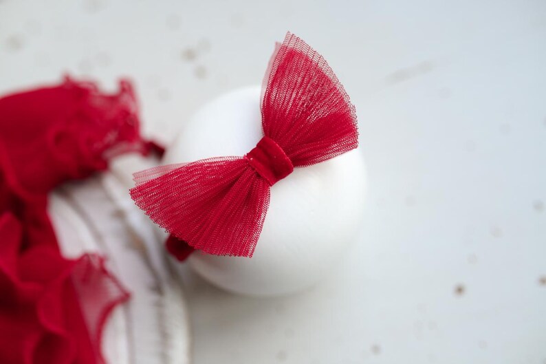 May include: A red tulle bow headband with a velvet center. The headband is on a white surface.