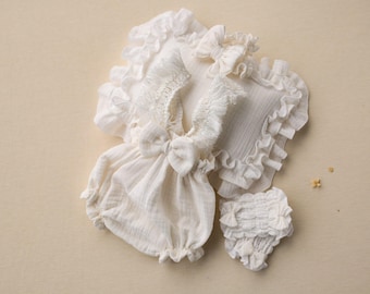 May include: A white baby outfit set with a ruffled top, a ruffled bottom, and a headband. The outfit is made of a soft, lightweight fabric and is perfect for a newborn baby.