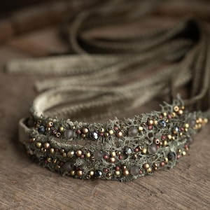 Könnte beinhalten: Ein zartes Stirnband aus Spitze, verziert mit kleinen Perlen und Strasssteinen. Das Stirnband ist hellbraun und hat einen Vintage-Look.