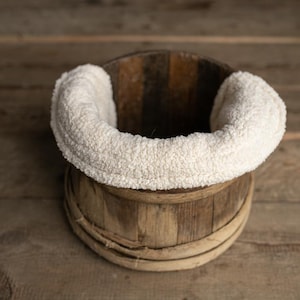 May include: A wooden bucket with a white fluffy fabric lining, perfect for newborn photography props.