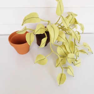 May include: A felt plant with green leaves in a brown pot. The plant is sitting on a white surface.