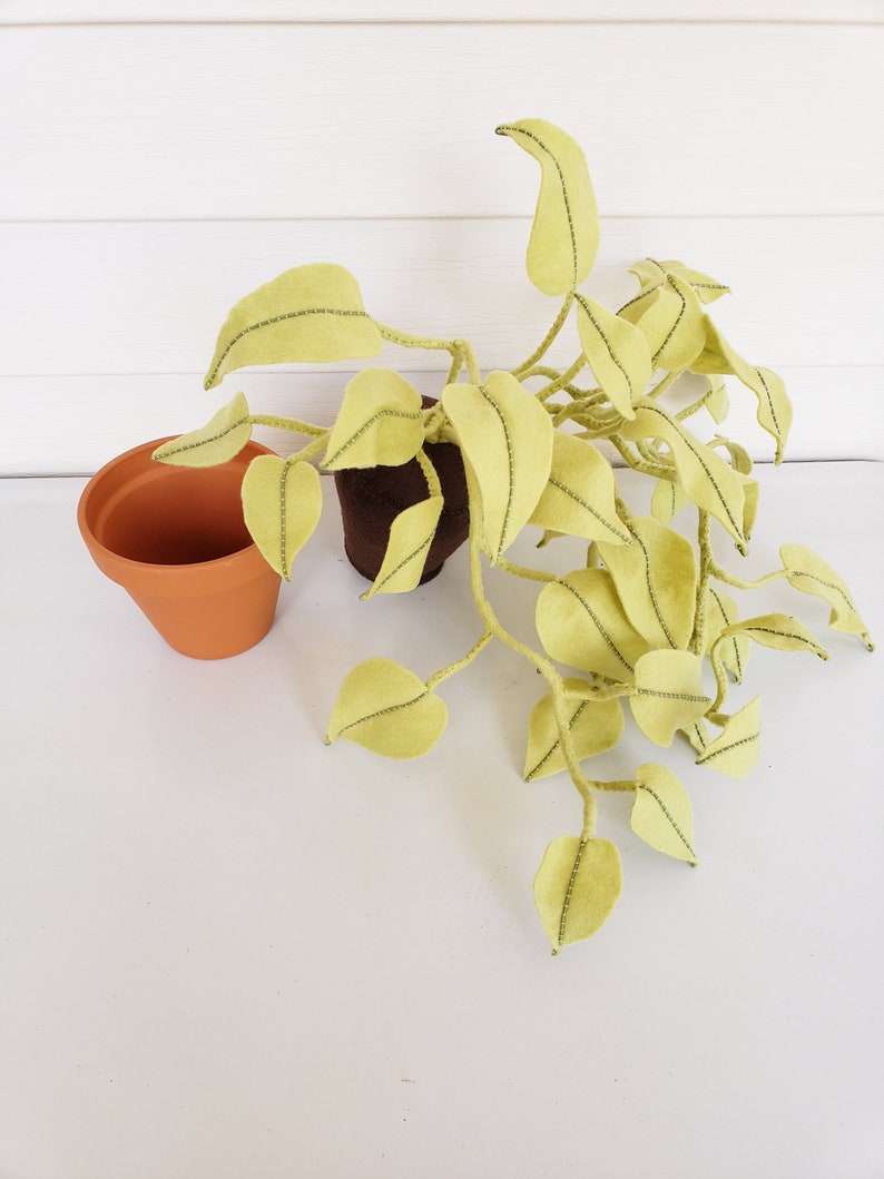 May include: A felt plant with green leaves in a brown pot. The plant is sitting on a white surface.