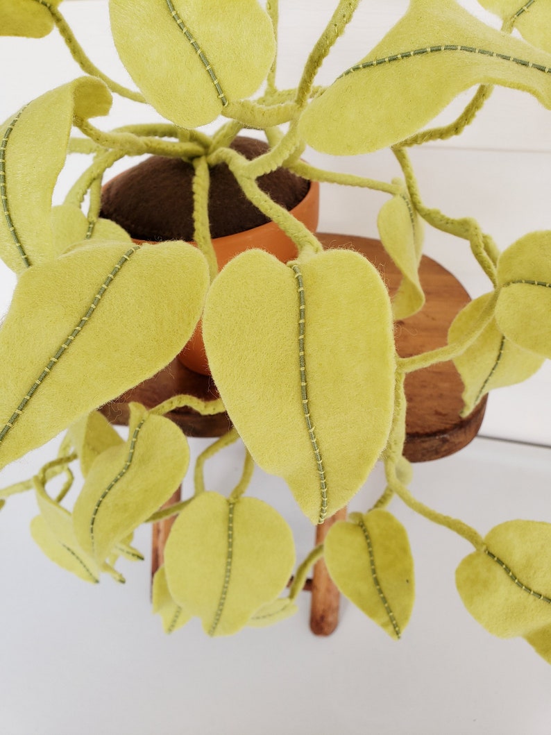 May include: A felt plant with green leaves and brown stems in a terracotta pot. The plant is sitting on a wooden stool.
