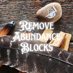 May include: A wooden background with a brown stone with a white symbol, a feather, and three pieces of palo santo wood. The text "REMOVE ABUNDANCE BLOCKS" is written in white on the image.