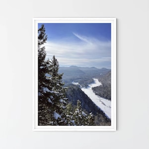 Può includere: Un paesaggio montano innevato con un fiume sinuoso nella valle. La scena è vista da un punto di vista elevato, con un gruppo di alberi sempreverdi in primo piano.