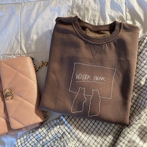May include: A brown sweatshirt with a white embroidered design of two bears sitting in front of a sign that says "Winter Bear".