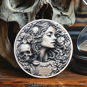 Puede incluir: Una moneda de plata con una escultura en relieve detallada de un rostro de mujer rodeado de flores y una calavera. La moneda tiene la inscripción "Ephemeral Beauty".