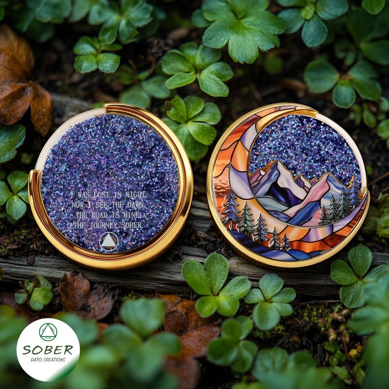 May include: Two round, gold-rimmed medallions. One features a glittery purple surface with the text "I WAS LOST IN NIGHT, NOW I SEE THE DAWN, THE ROAD IS MINE, THE JOURNEY SOBER." The other depicts a mountain scene within a crescent moon.