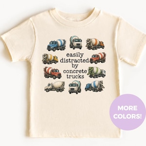 May include: A cream-colored short-sleeve t-shirt featuring a circular arrangement of eight different concrete mixer trucks surrounding the black text that reads, easily distracted by concrete trucks. The design is centered on the front of the shirt.
