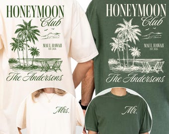 May include: Ivory and moss green t-shirts with a tropical design. The shirts feature the text "HONEYMOON CLUB" above a palm tree illustration and "MAUI, HAWAII" with "The Andersons" below. One shirt says "Mrs." and the other says "Mr."