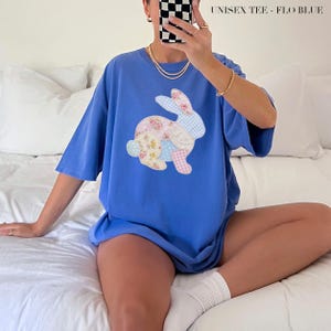 May include: A flo blue short-sleeved t-shirt featuring a central graphic of a rabbit composed of various patchwork fabric patterns, including floral, gingham, and polka dot prints in soft pastel colours. The text UNISEX TEE - FLO BLUE is visible.