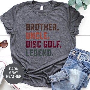 Może przedstawiać: Szary t-shirt w kolorze melanżu z nadrukiem "Brother. Uncle. Disc Golf. Legend." w stylu vintage.