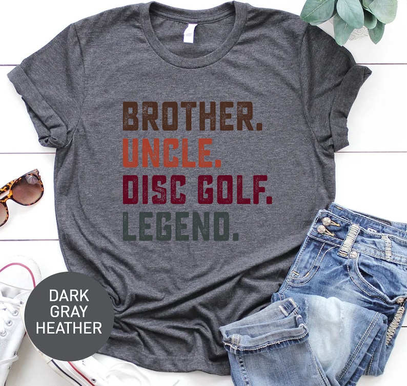 Może przedstawiać: Szary t-shirt w kolorze melanżu z nadrukiem "Brother. Uncle. Disc Golf. Legend." w stylu vintage.