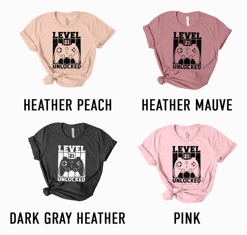 May include: Four t-shirts in different colors with a graphic of a video game controller and the text "Level 21 Unlocked". The colors are heather peach, heather mauve, dark gray heather, and pink.