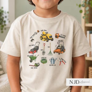 Pode incluir: Uma t-shirt bege com uma impressão gráfica de várias ferramentas de jardinagem e paisagismo, incluindo um trator corta-relva, um corta-relva de giro zero, um corta-relva manual, um aparador, um soprador, um carrinho de mão, uma pá, um ancinho, uma mangueira, um regador e tesouras de poda.