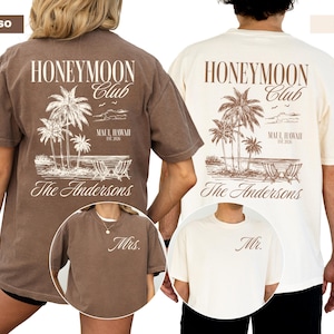 two t-shirts with the same design, one for a man and one for a woman. The design includes palm trees, chairs, and a beach scene. The text on the t-shirts reads "Honeymoon Club" and "The Andersons".