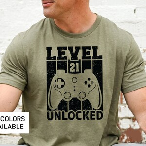 May include: A green t-shirt with a black graphic design that says "Level 21 Unlocked" with a video game controller graphic.