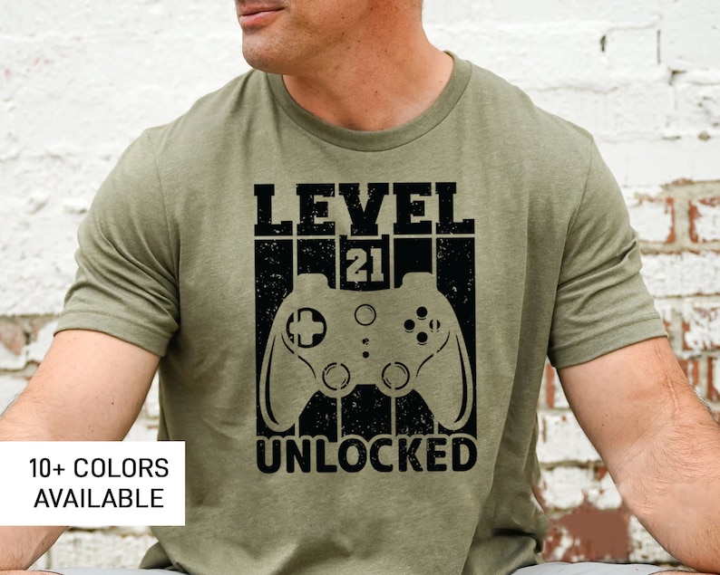 May include: A green t-shirt with a black graphic design that says "Level 21 Unlocked" with a video game controller graphic.