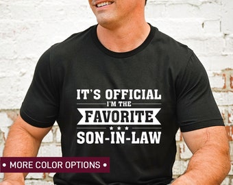 May include: Black t-shirt with white text that reads "It's Official I'm the Favorite Son-in-Law" with three stars between "Favorite" and "Son-in-Law".