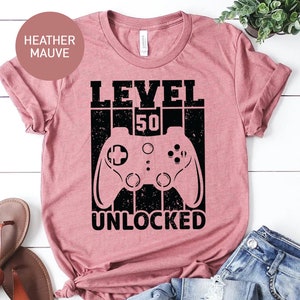 May include: Heather mauve t-shirt with a black graphic of a video game controller and the text "LEVEL 50 UNLOCKED".