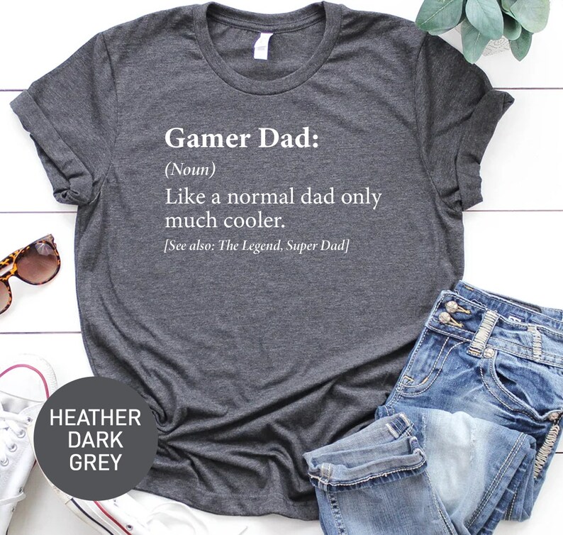 May include: Heather dark grey t-shirt with the text "Gamer Dad: (Noun) Like a normal dad only much cooler. [See also: The Legend, Super Dad]" printed in white.