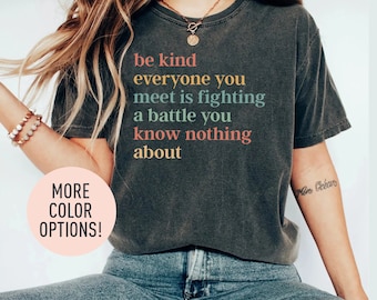 May include: A dark gray t-shirt with the text "be kind everyone you meet is fighting a battle you know nothing about" printed in rainbow colors.