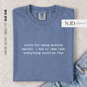 May include: A blue short-sleeved t-shirt with a crew neckline. The shirt features white text printed on the chest that reads: sorry for being anxious earlier, i had no idea that everything would be fine. The garment has a Comfort Colors brand label.