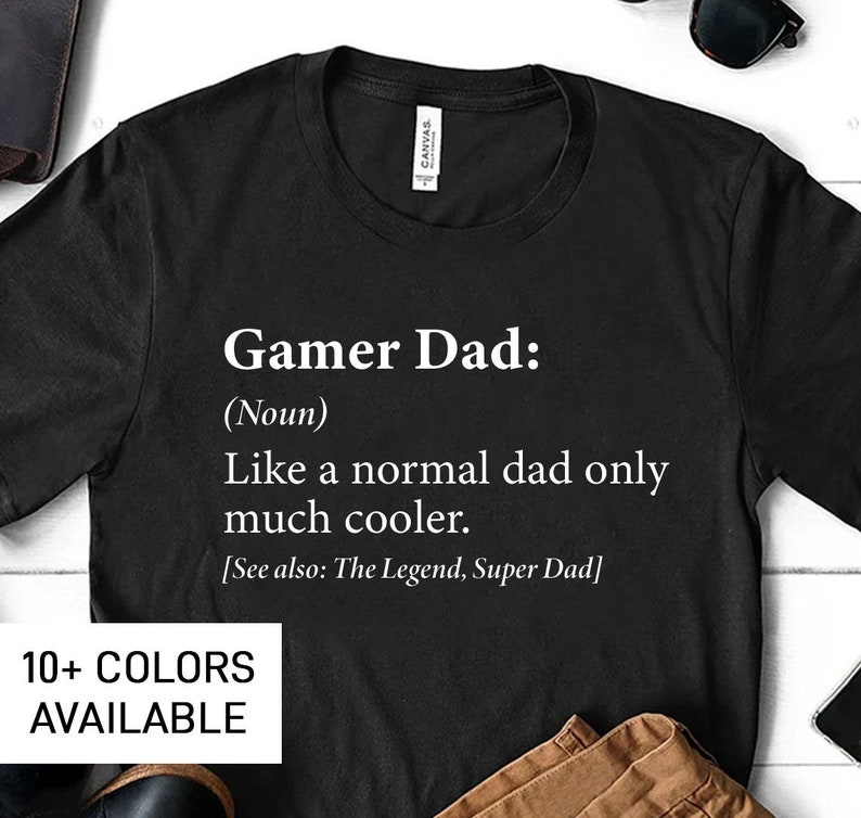 May include: Black t-shirt with white text that reads "Gamer Dad: (Noun) Like a normal dad only much cooler. [See also: The Legend, Super Dad]"  10+ COLORS AVAILABLE