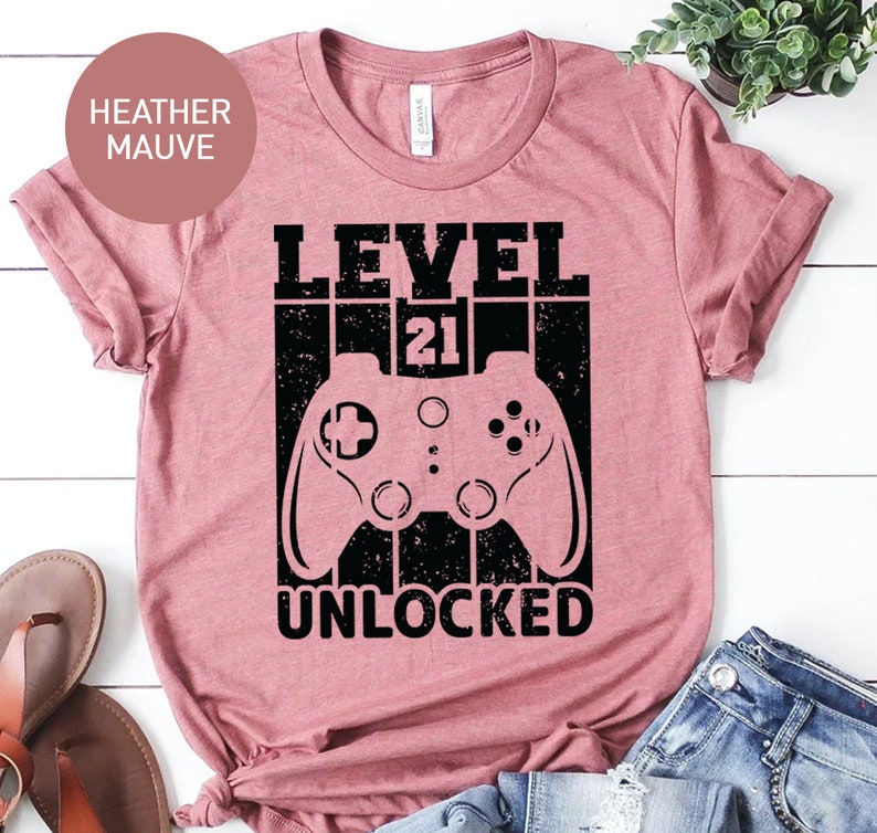 May include: Heather mauve t-shirt with a black graphic of a video game controller and the text "LEVEL 21 UNLOCKED".