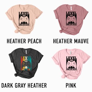 May include: Four different color t-shirts with a retro video game controller graphic and the text "Level 40 Unlocked". The colors are heather peach, heather mauve, dark gray heather, and pink.