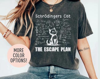 May include: A dark gray t-shirt with a white graphic of a cat and scientific formulas. The text "Schrödingers Cat" and "The Escape Plan" are printed on the shirt.