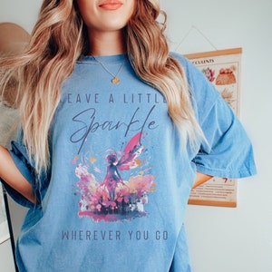 May include: A light blue oversized t-shirt with a graphic of a fairy with wings and the text "Leave a Little Sparkle Wherever You Go".