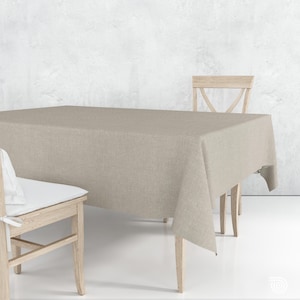 Peut inclure: Une nappe rectangulaire beige recouvrant une table en bois, avec une chaise assortie de chaque côté. La nappe a un aspect texturé et les chaises ont des cadres en bois de couleur claire. Un coussin blanc est posé sur une chaise.
