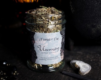 Puede incluir: Un frasco de vidrio lleno de hierbas secas etiquetado "of Forest and Fae Uncrossing spellwork herb blend" para la inversión de hechizos, la ruptura de hechizos, el retorno al remitente.