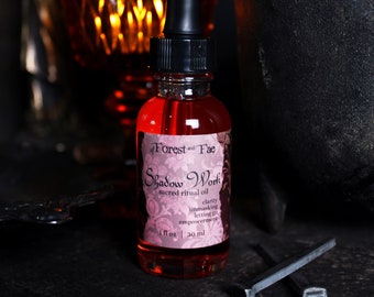 Può includere: Una piccola bottiglia di vetro rossa con un contagocce. La bottiglia è etichettata "of Forest and Fae Shadow Work sacred ritual oil clarity unmasking letting go empowerment 1 fl oz | 30 ml".