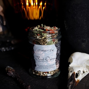 May include: A glass jar filled with a blend of dried herbs and flowers labeled "Road Opener spellwork herb blend" by "of Forest and Fae". The label describes the blend as being for opportunity, removing obstacles, good fortune, success, and clearing blockages.