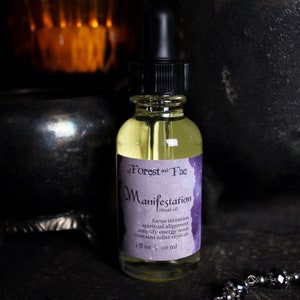 May include: A glass bottle of Manifestation ritual oil with a purple label that reads "of Forest and Fae" and "Manifestation ritual oil" with the text "focus intention, spiritual alignment, amplify energy work, contains iolite crystals, 1 fl oz | 30 ml".
