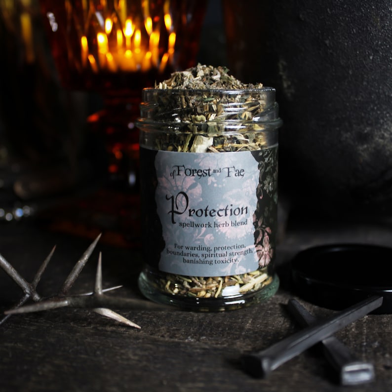 K&ouml;nnte beinhalten: Ein Glasgef&auml;&szlig; gef&uuml;llt mit getrockneten Kr&auml;utern, beschriftet mit "Protection spellwork herb blend" von "of Forest and Fae". Das Etikett besagt auch "F&uuml;r Schutz, Grenzen, spirituelle St&auml;rke, Beseitigung von Toxizit&auml;t."
