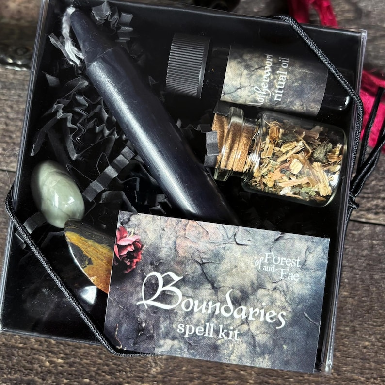 K&ouml;nnte beinhalten: Eine schwarze Box mit einer schwarzen Kerze, einer kleinen &Ouml;lflasche, einem kleinen Glas mit Kr&auml;utern und einer Karte mit der Aufschrift "Boundaries spell kit" mit den Worten "Forest and Fae". Die Box enth&auml;lt auch einen gr&uuml;nen Stein und einen schwarzen Stein.