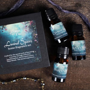May include: A home fragrance set with three essential oil blends in amber glass bottles. The set includes a black box with the text "Liminal Spaces home fragrance set" and the brand name "Forest and Fae". The bottles are labeled "Crossroads", "Reflection", and "Shapeshift".