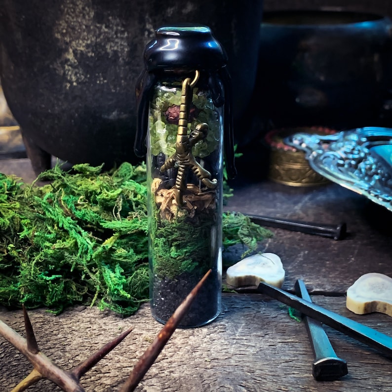 May include: A small glass bottle filled with green, black, and brown materials. A gold scorpion charm hangs from the top of the bottle.
