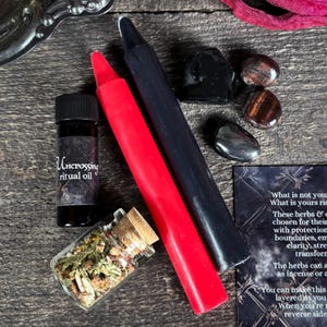 May include: A black and red candle set, a small bottle of oil labeled "Uncrossing ritual oil", a small jar of dried herbs, and several black and brown stones. The text on the card reads "What is not yours rise, What is yours rise, These herbs & crystals are chosen for their protective properties with protection for boundaries, empowerment, clarity, strength, transformation. The herbs can be used as incense or a bath. You can make this layered as you wish. When you're ready, reverse side."
