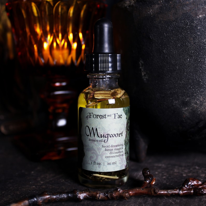 Puede incluir: Una peque&ntilde;a botella de vidrio con un gotero negro en la parte superior, llena de un l&iacute;quido amarillo y hierbas secas. La etiqueta dice "of Forest and Fae Mugwort dream oil lucid dreaming lunar magick divination consecration 1 fl oz | 30 ml".