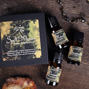 May include: A home fragrance set with three essential oil bottles and a box. The box reads "Spell Weaver home fragrance set" with the text "Forest and Fae". The bottles are labeled "Ritual", "Incantation", and "Conjure". The set is on a wooden surface.