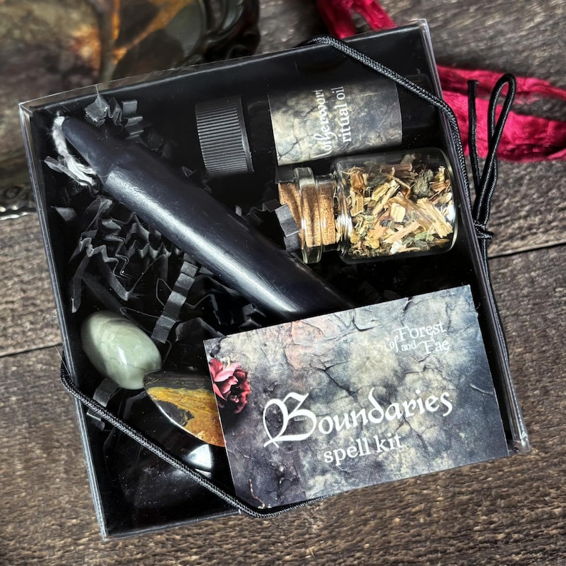 K&ouml;nnte beinhalten: Eine schwarze Box mit einer schwarzen Kerze, kleinen Flaschen, Kristallen und einer Karte. Auf der Karte steht "Boundaries spell kit" mit "Forest and Fae" dar&uuml;ber. Die Box ist mit schwarzem Papier gef&uuml;llt.