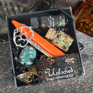 May include: A black box with a silver key, an orange candle, a small bottle of oil, a small jar of herbs, and a green stone. The box has a label that says "Unlocked road opening kit" and "Forest of the Fae".