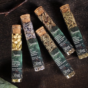 May include: Five glass vials with cork stoppers, each filled with dried herbs. The vials are labeled "Jasmine," "Lavender," "Damiana," "Mugwort," and "Rosemary." Each label includes the herb's properties and the words "Forest and Fae."